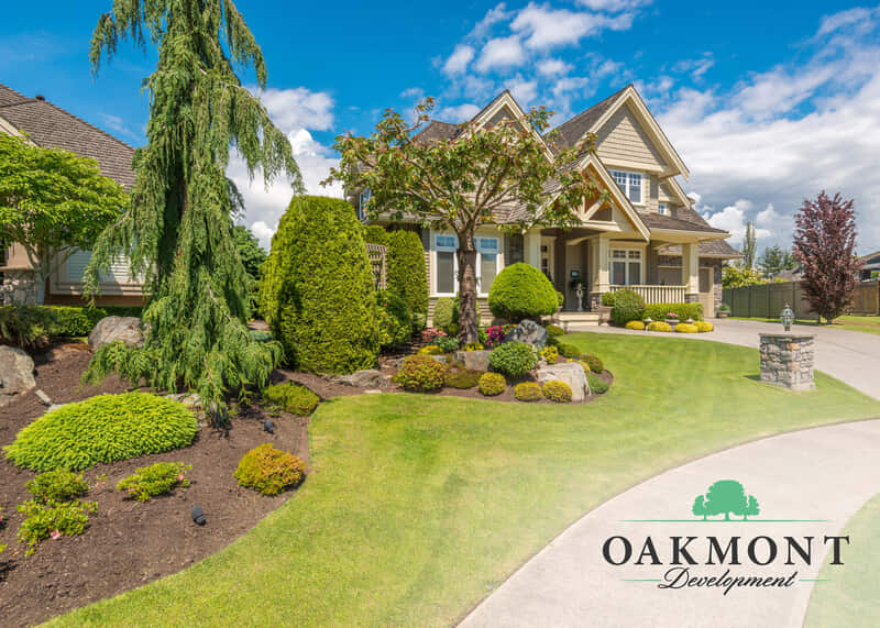 A landscaped yard with trees and flows with a house in the background